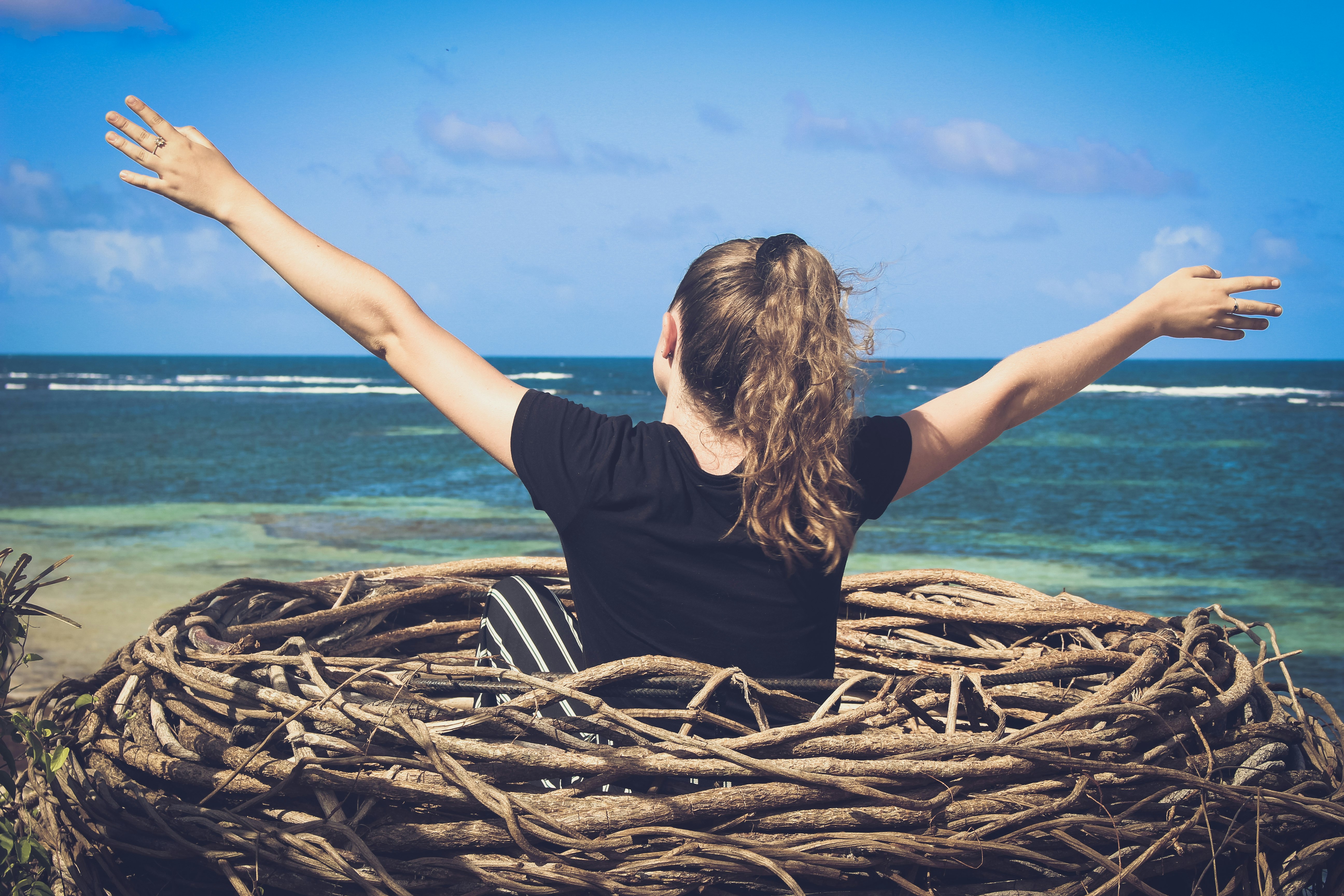 woman in black shirt sitting on brown wooden log near body of water during daytime